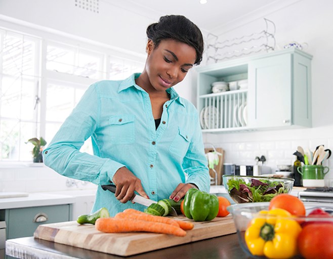 Woman in kitchen cutting fresh vegetables with knife