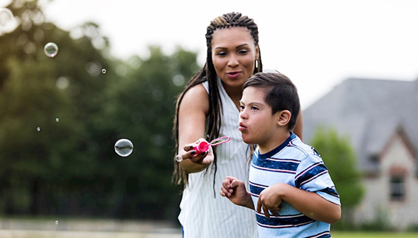 Woman outside with her young son helping him blow bubbles