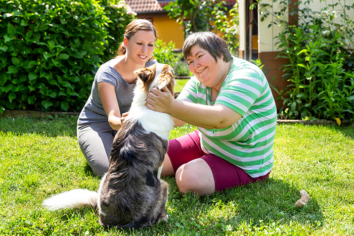 Two women sitting in grass outside petting a dog