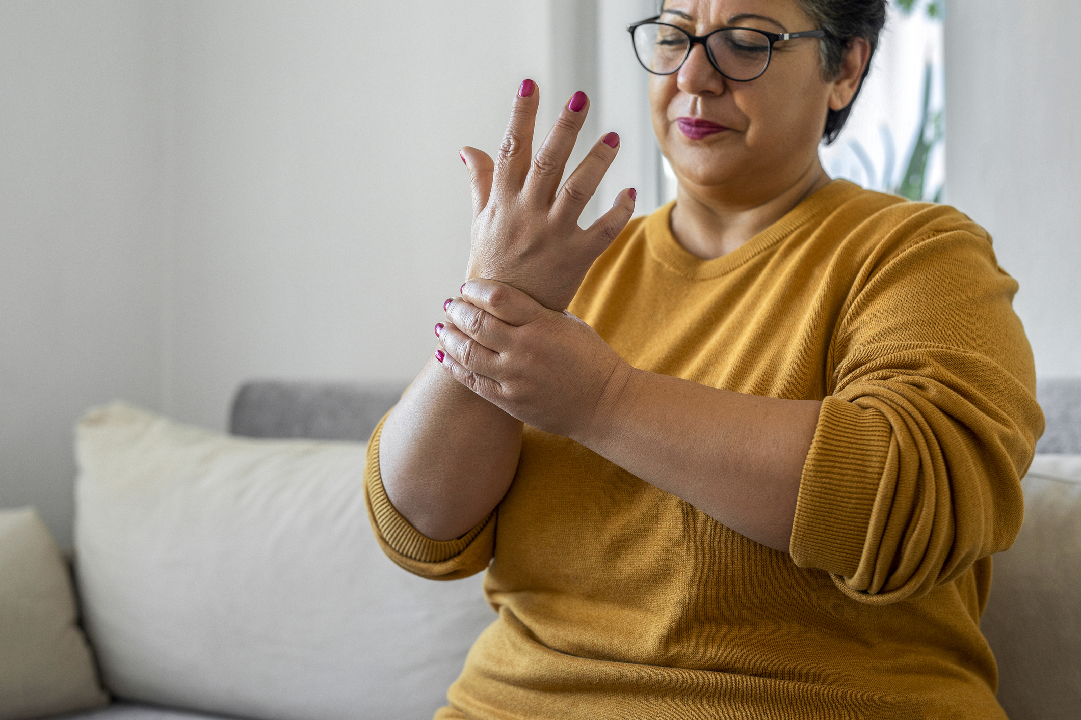 Woman sitting on couch and holding her wrist