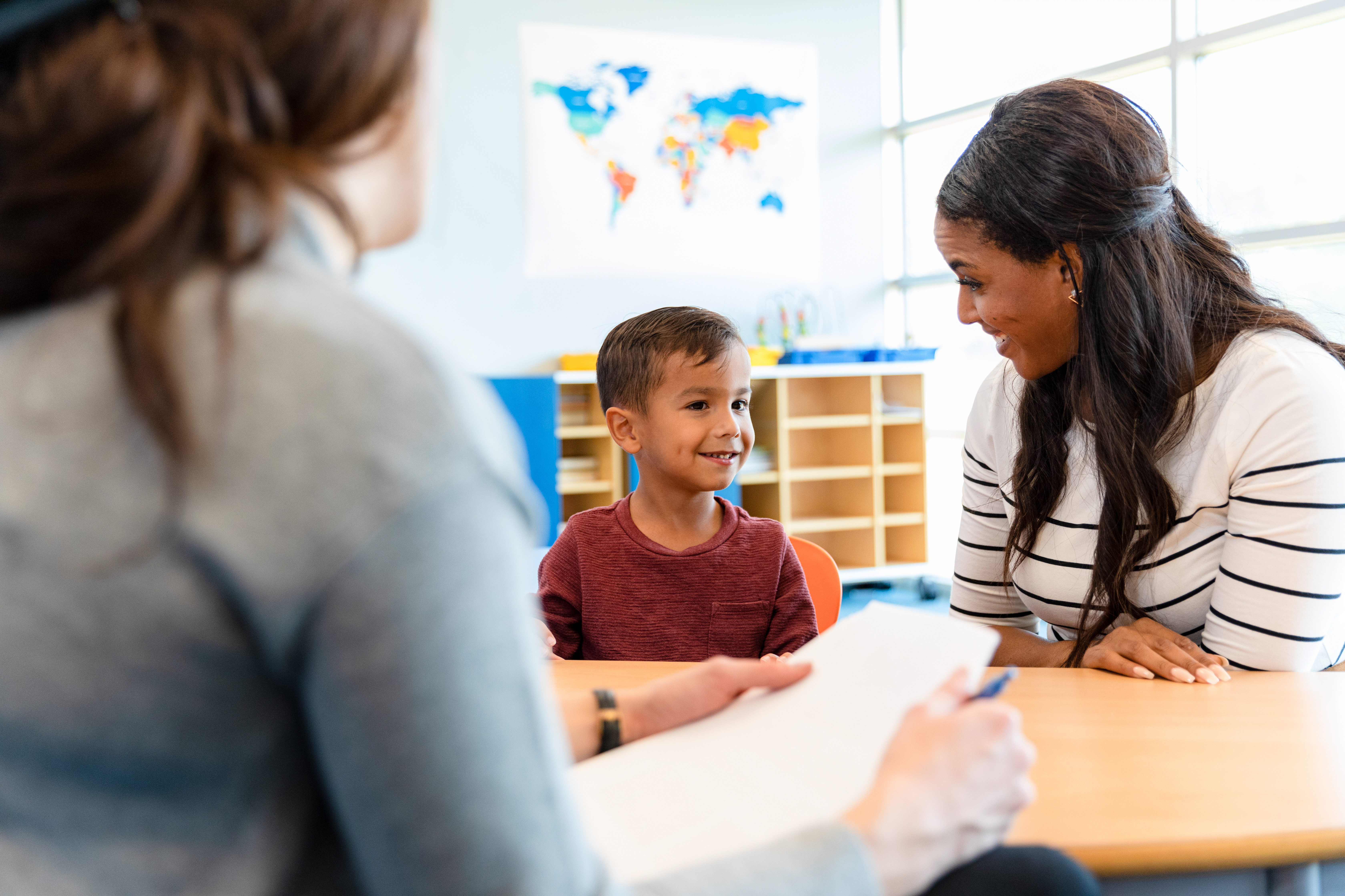 Young boy in schools with teacher and adult taking notes
