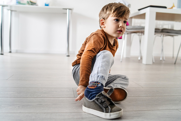 Small child sitting on floor putting shoes on