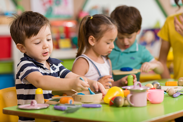 Three preschool aged kids sitting at classroom table playing with various toys