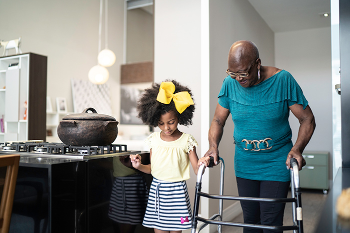 Young girl walking beside senior woman using walker through kitchen