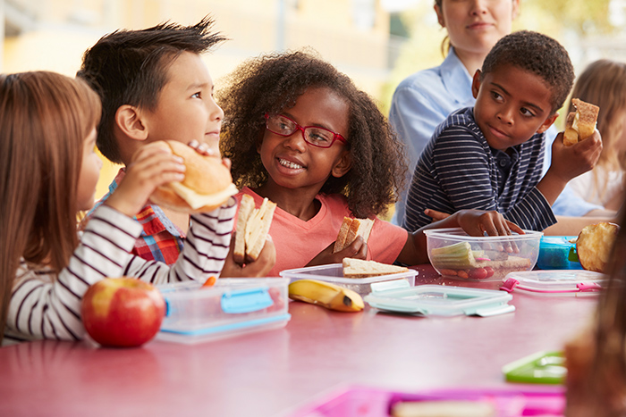 School aged kids sitting at cafeteria table eating together
