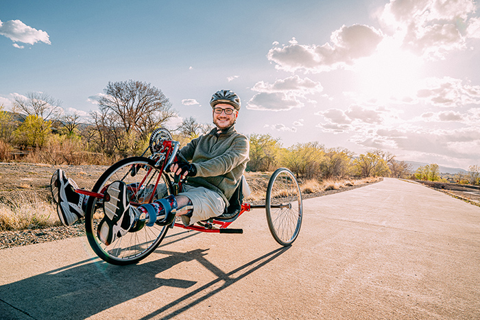 Man outside wearing helmet and leg braces riding handcycle