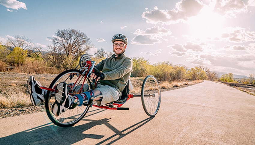 Man outside wearing helmet and leg braces riding handcycle