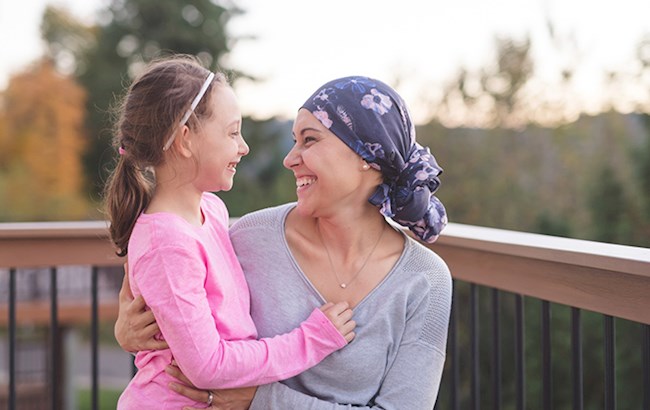 Woman wearing headscarf smiling and embracing young girl outside on deck