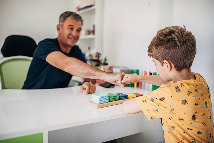 Man and young boy fist bumping across a desk inside classroom