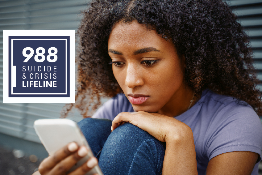 Young woman looking at cellphone while sitting on the ground. Logo to the left reads 988 Suicide and Crisis Lifeline