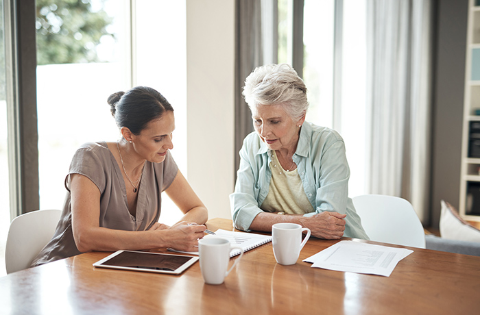 Woman helping older woman with paperwork while sitting at table
