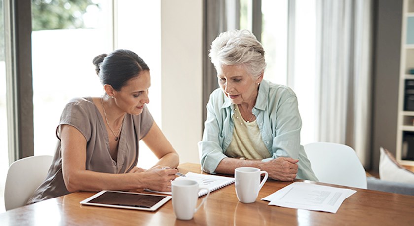 Woman helping older woman with paperwork while sitting at table