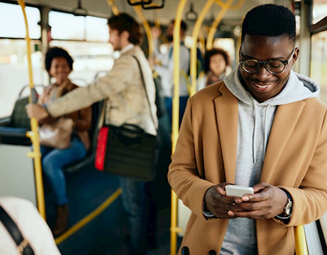 Smiling man reading phone while standing in public bus