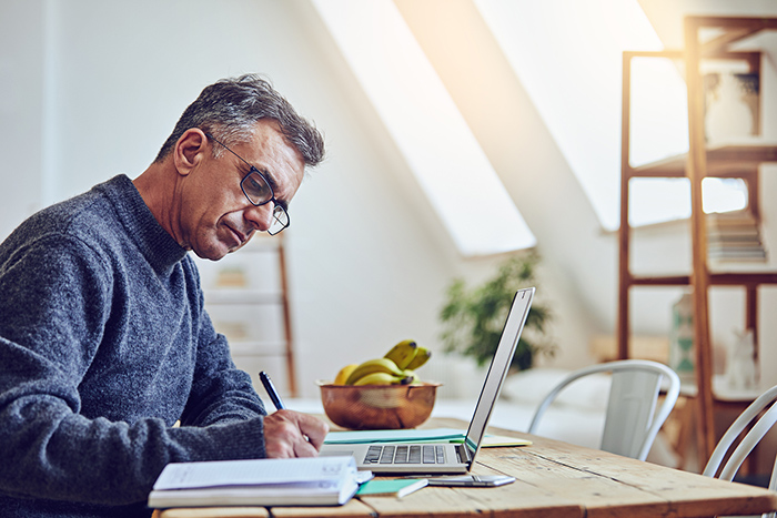 Man working at desk with open laptop and writing in notebook