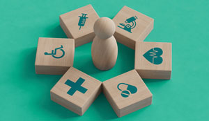 Wooden cubes in a circle around a wooden figure. The cubes have medical symbols on them, such as a wheelchair, a heart, and a syringe.