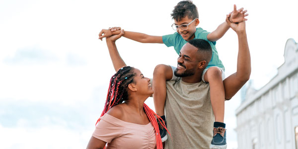 A small family made up of mom, dad, and son. The boy is on his dad's shoulders.