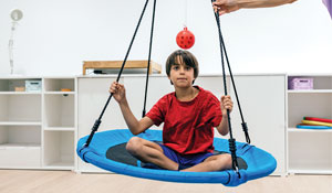 Child sitting on an indoor round swing that is close to the floor.