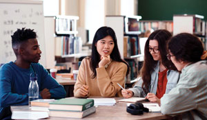 Students sitting around a table with books on it, intently talking with each other.