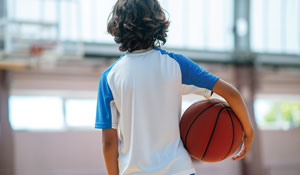 Young boy walking away from the camera holding a basketball under his right arm.