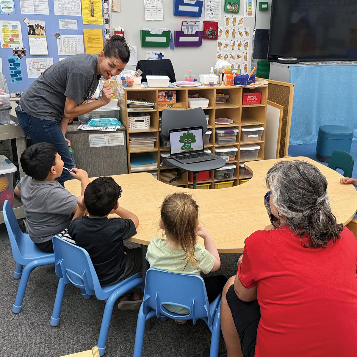 A preschool teacher of students with Level 2 and level 3 Autism passing out toothbrushes to her students as they begin circle time toothbrushing