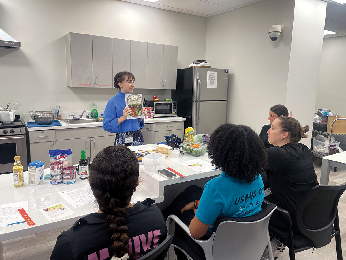 Brittani Ivan providing sharing her favorite Bento Box recipe book with students. From left to right (Melisa, Jazmin, Stephanie, and Samantha)