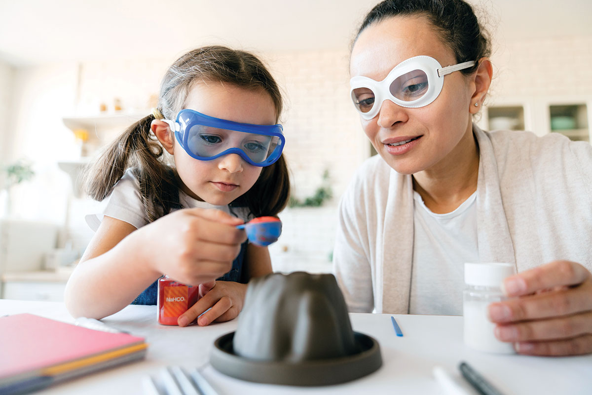 A teacher and student wearing safety glasses and creating a small volcano