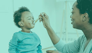 A mom smiling and feeding her young child with a spoon