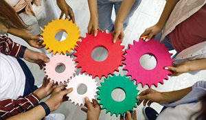 Diverse human arms holding colorful gears together