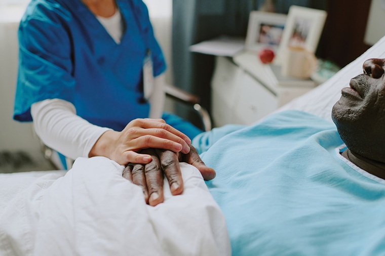 Nurse putting hand on patient's hand who is lying in a hospital bed