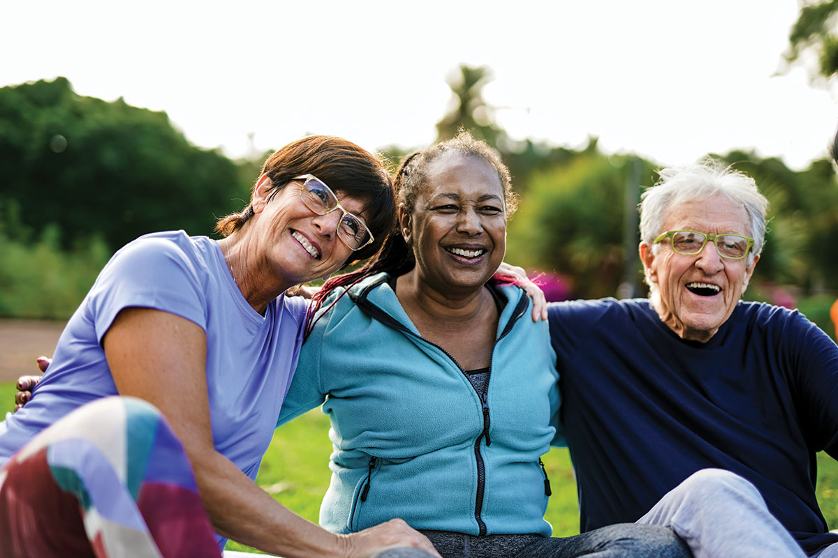 Three older adults, smiling, in workout clothes, with their arms around each other