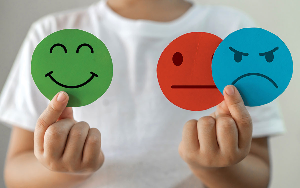 Round happy, neutral, and angry face circles in green, red, and blue being held by a person in a white tee.