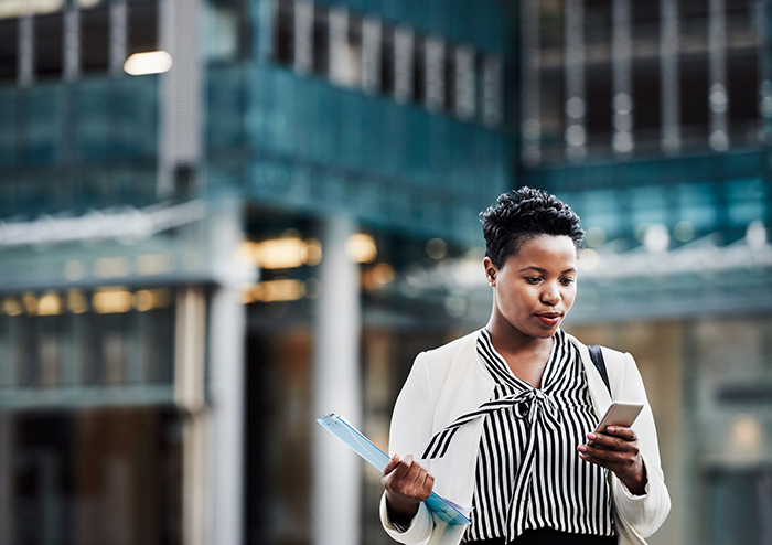 Professional woman outside holding binder and reading cell phone