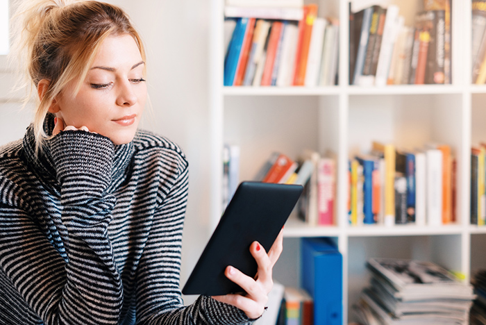 Woman reading eReader with bookcase behind her