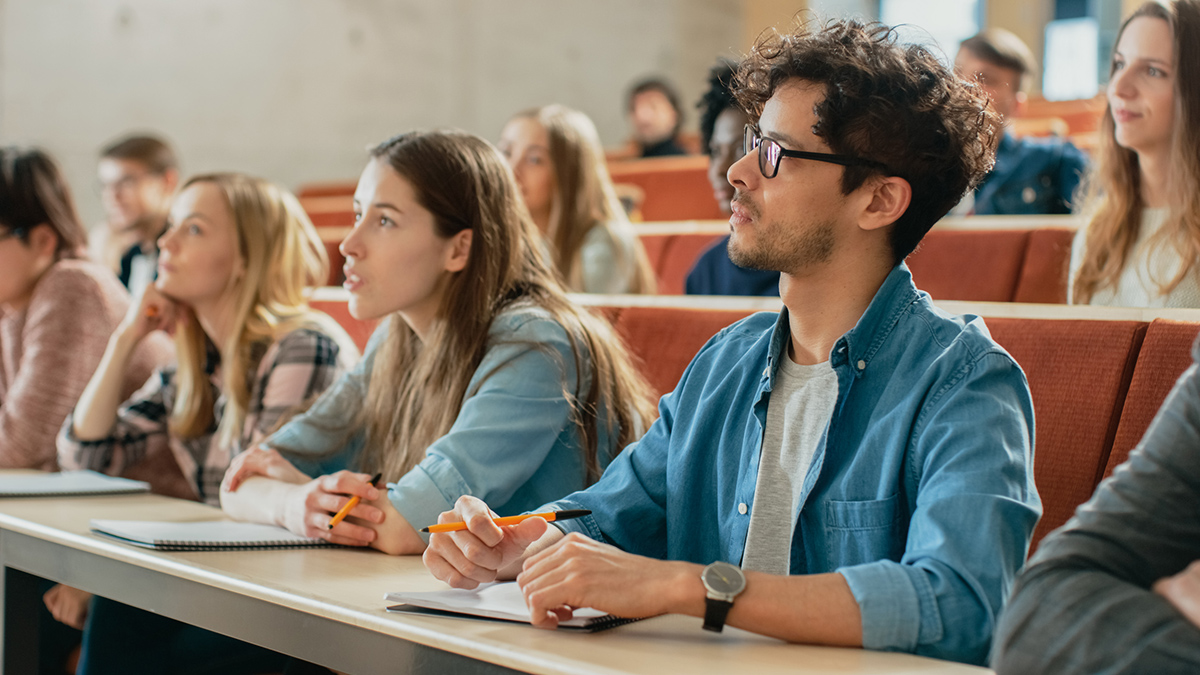 College students listing to lecture inside lecture hall with open notebooks