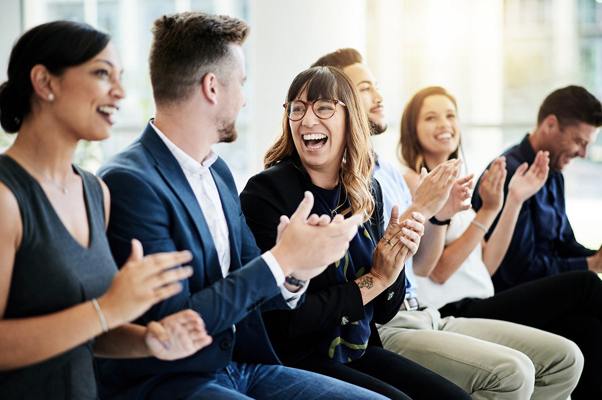 Group of people clapping at event with focus on woman wearing glasses