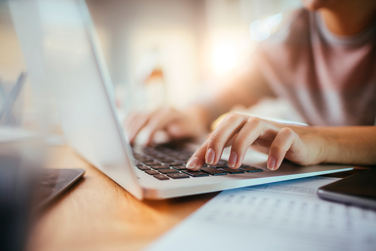 Close up of female hands typing on a laptop keyboard with paperwork on the desk