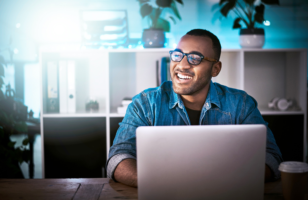 Man wearing glasses smiling while using laptop in home office