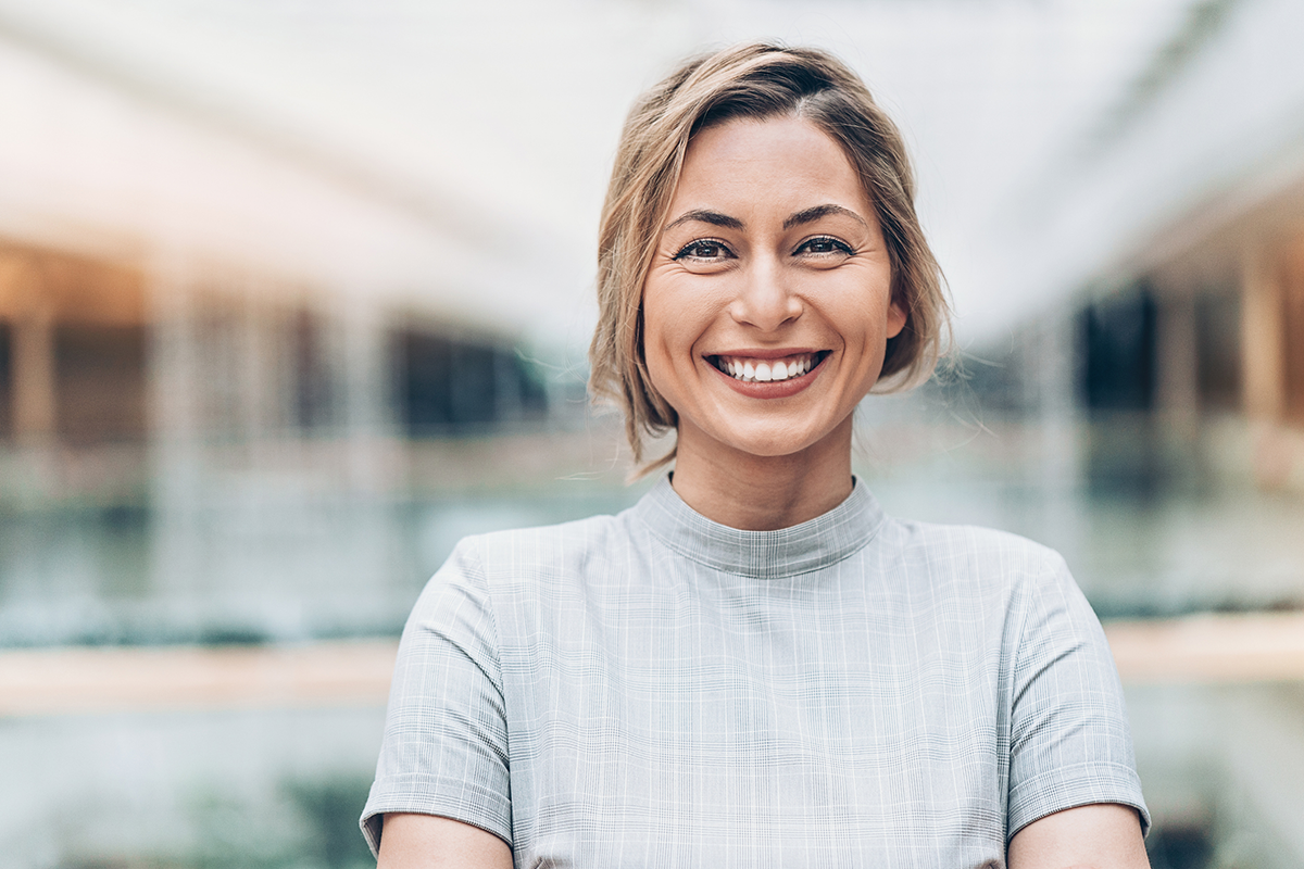 Professionally dressed woman with arms crossed smiling at camera in front of blurred background