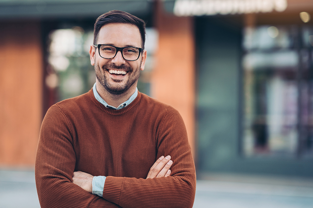 Smiling professional man with arms crossed outside in front of building looking at camera