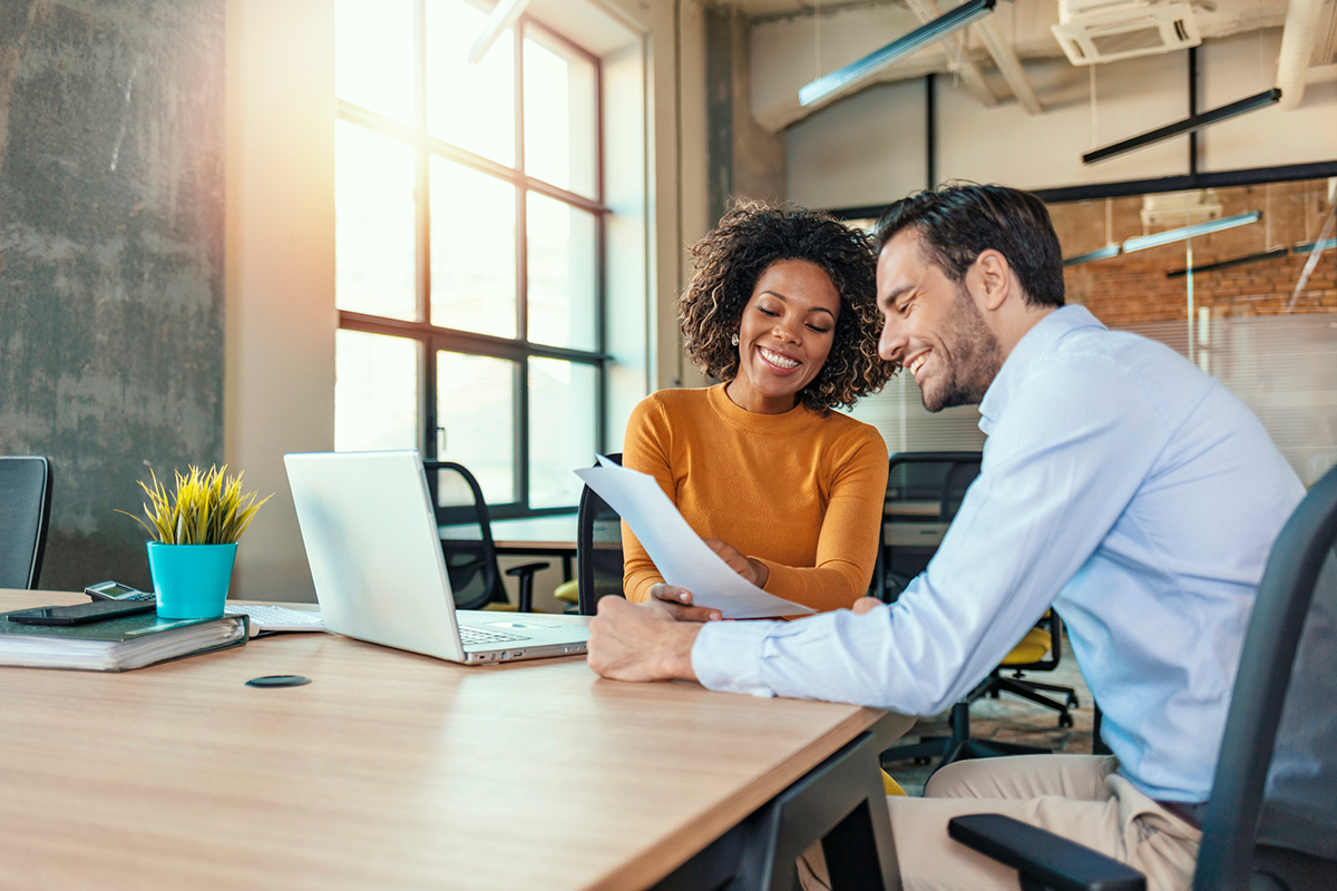 Man and woman sitting at table in an office smiling while looking over official paperwork
