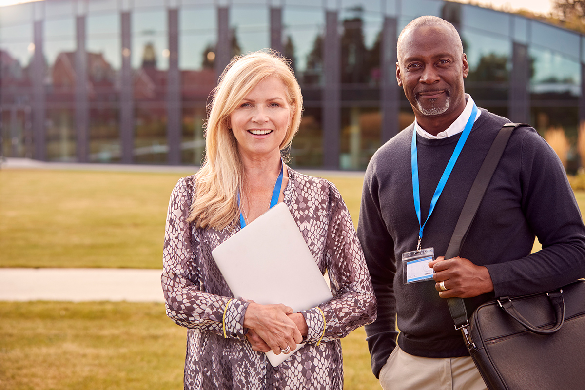 Professional woman and man wearing conference badges standing outside building smiling
