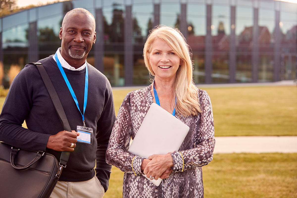Smiling man and woman wearing conference badges standing outside building looking at camera