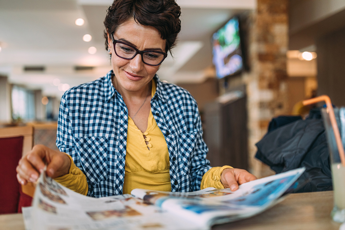 Smiling woman wearing casual clothes reading a magazine at a table