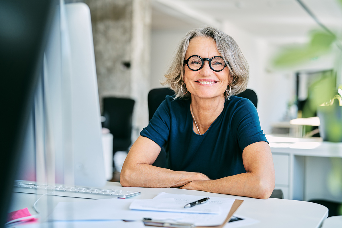 Mature woman smiling at desk while doing documentation paperwork