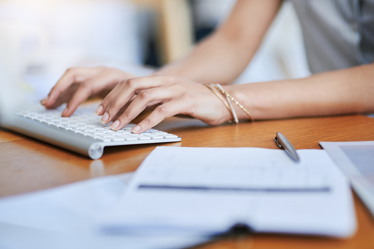 Close up of female hands typing on computer keyboard with billing paperwork on tablet