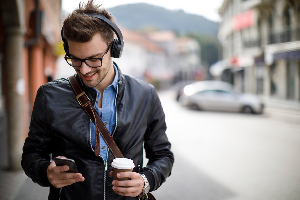 Man outside walking wearing headphones and listening to podcast while drinking coffee