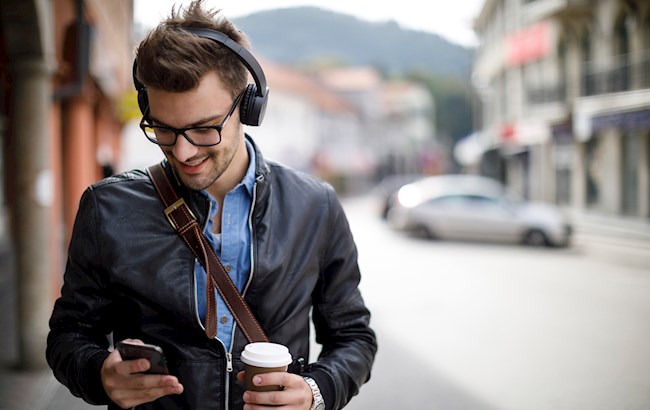 Man outside walking wearing headphones and listening to podcast while drinking coffee