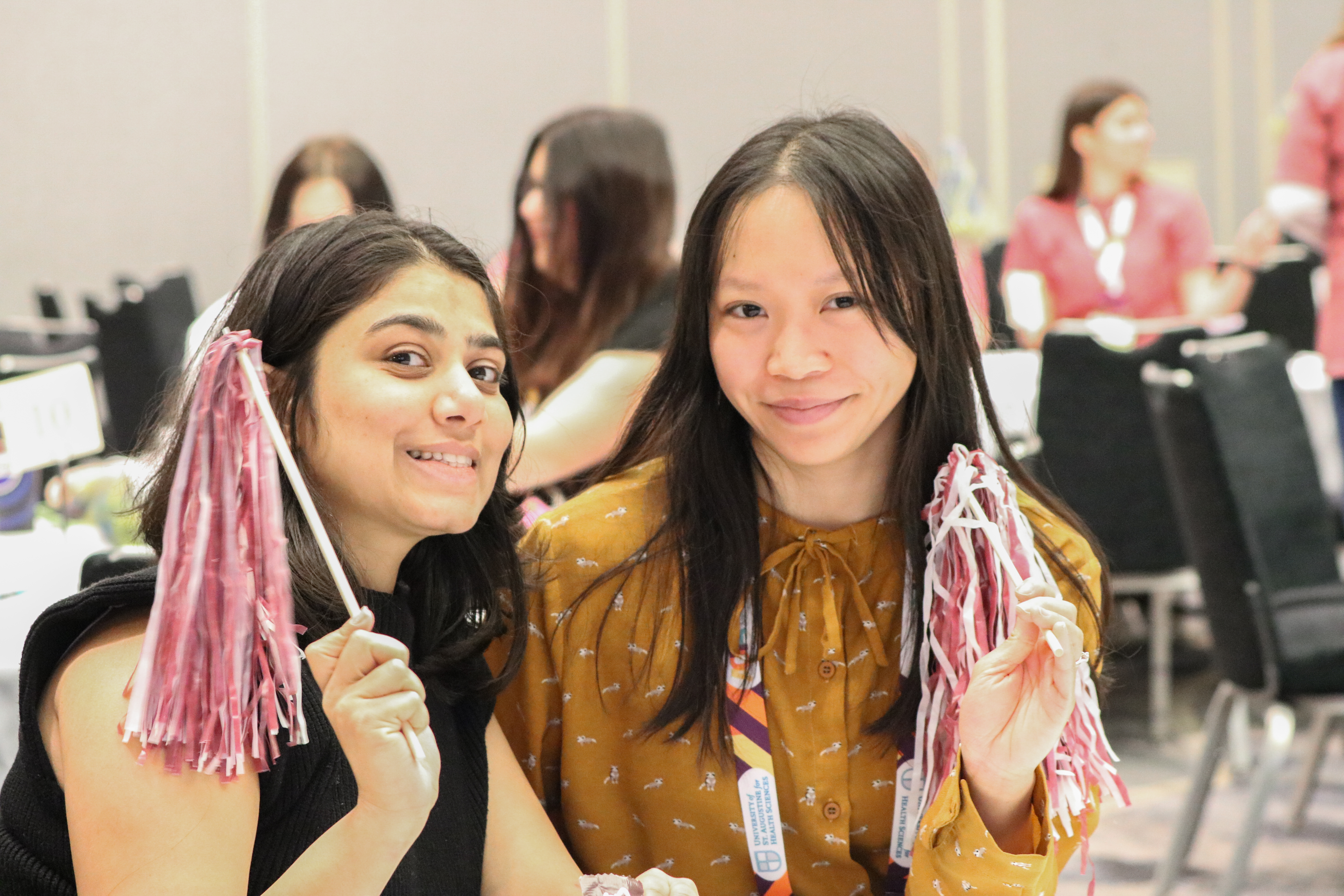 Two women sitting at a table holding pom-poms.