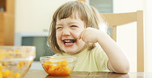 A little girl laughing and eating fruit.