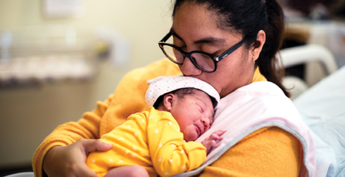Woman with glasses holding baby on her shoulder